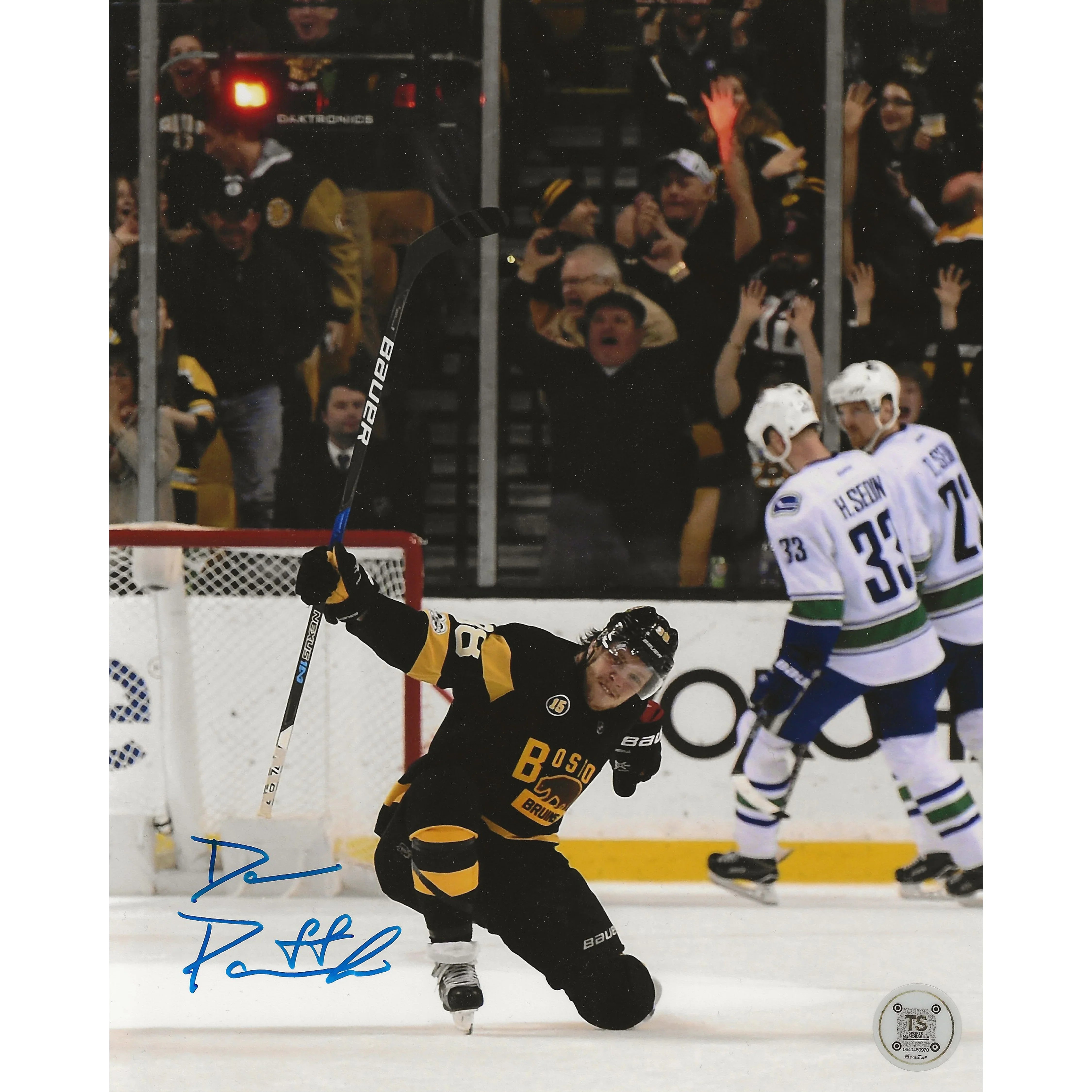 Boston Bruins hockey player celebrating goal on ice with fans cheering, Vancouver Canucks players behind