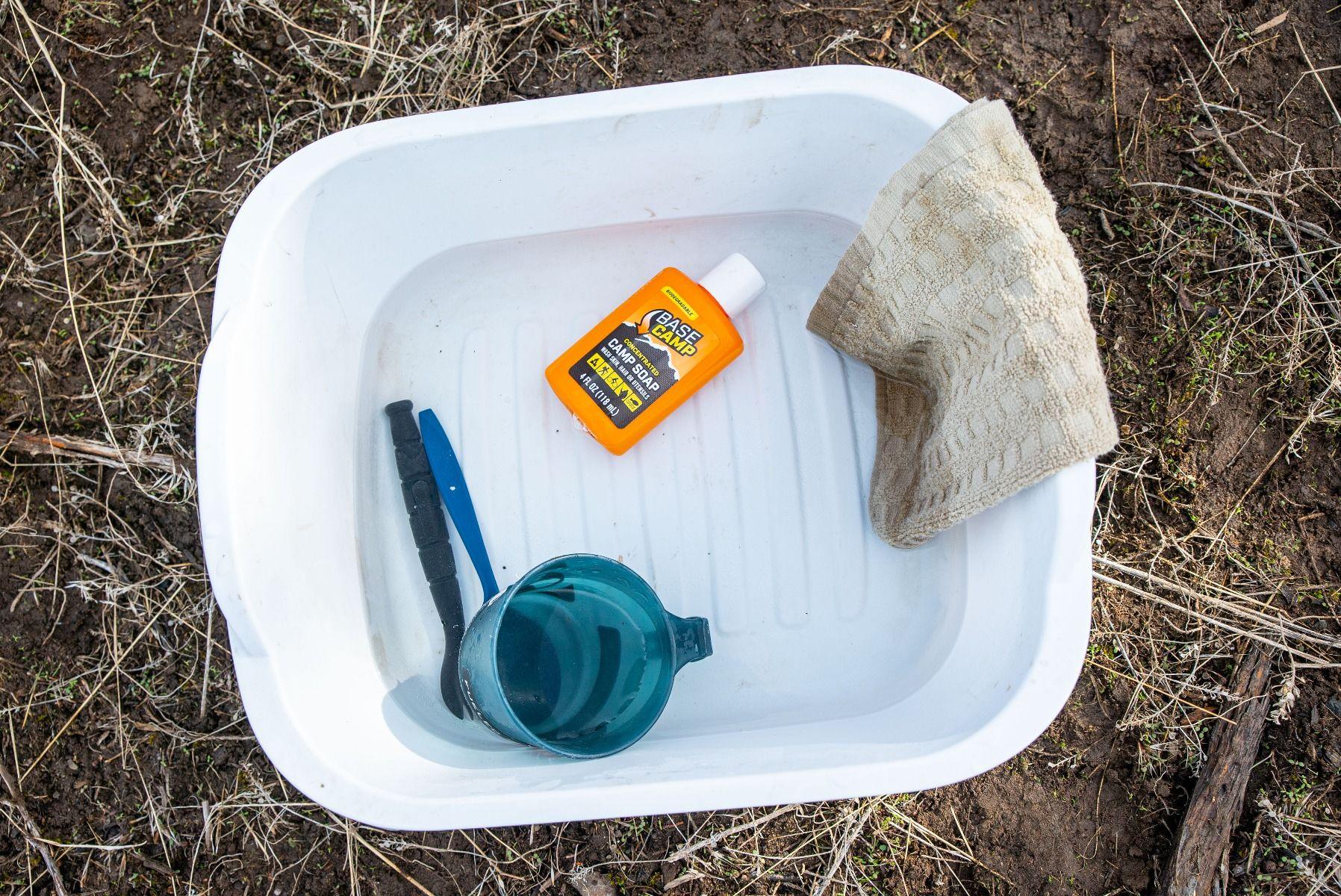 White camp wash basin with Base Camp soap, blue cup, utensil, and tan towel outdoors