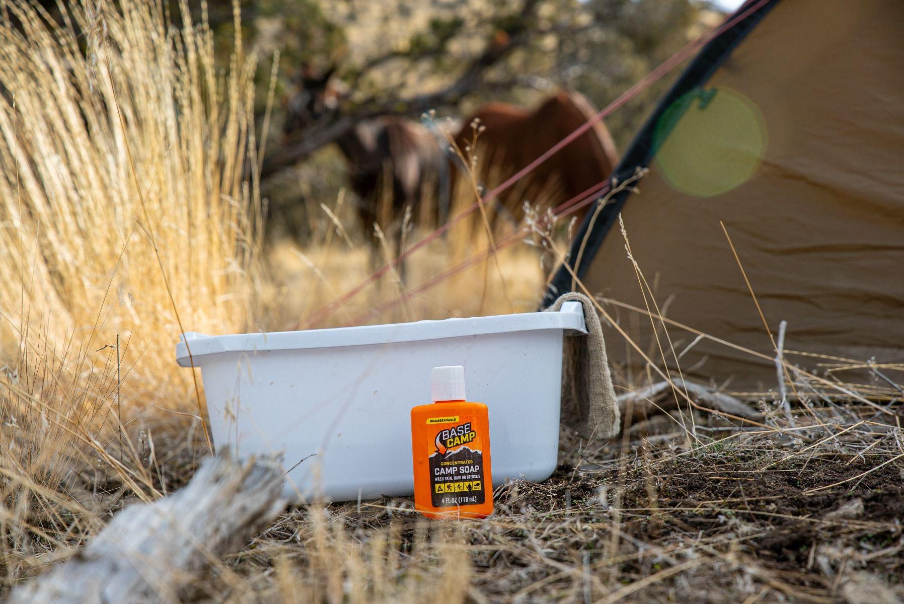 Base Camp camp soap bottle and white tub outdoors by tent and horses in dry grass