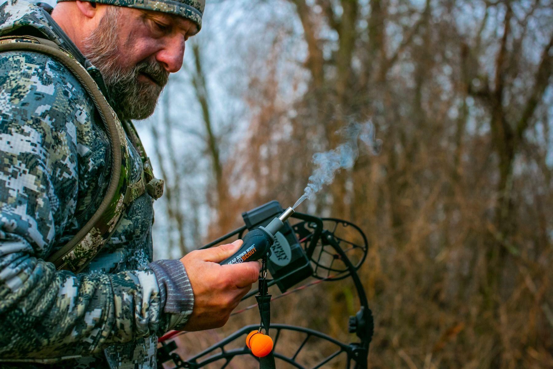 Hunter in camo using Dead Down Wind Wind Scout scent device outdoors with compound bow