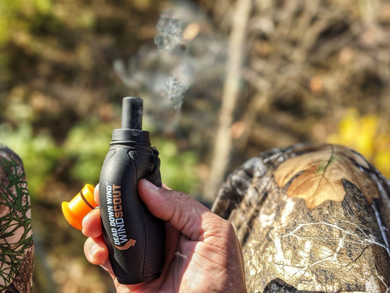 Hand holding Dead Down Wind Wind Scout scent checker outdoors, camouflage gear visible
