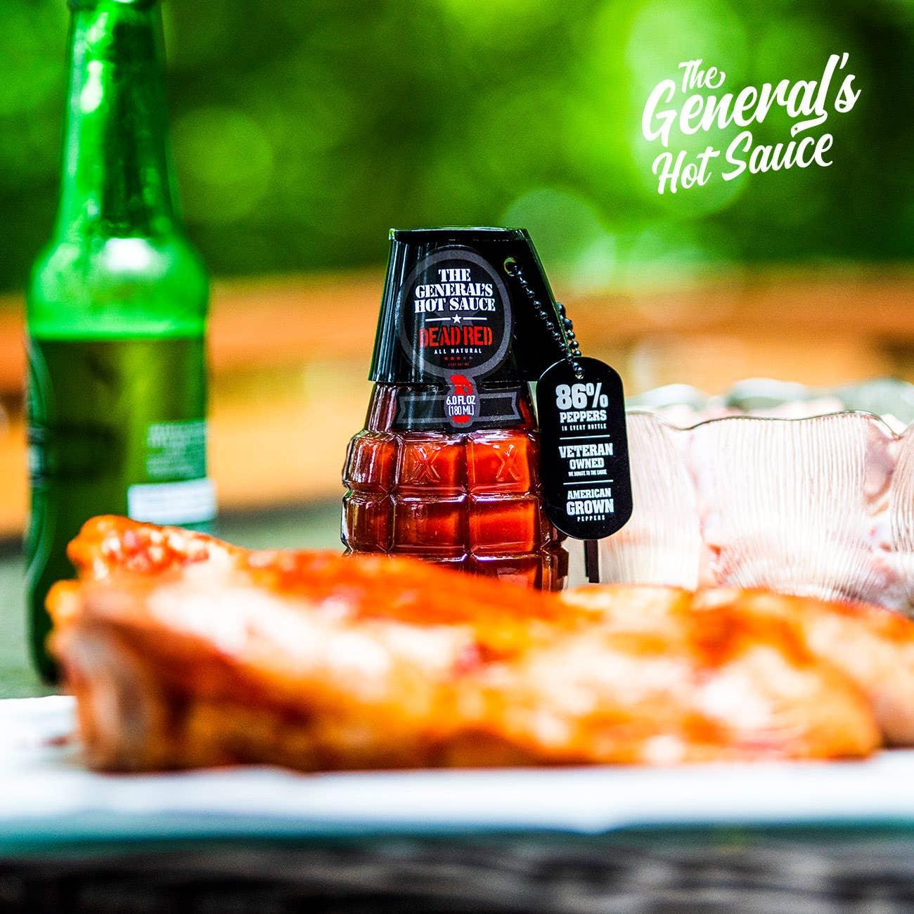 The General's Hot Sauce grenade-shaped bottle on outdoor table with beer and food