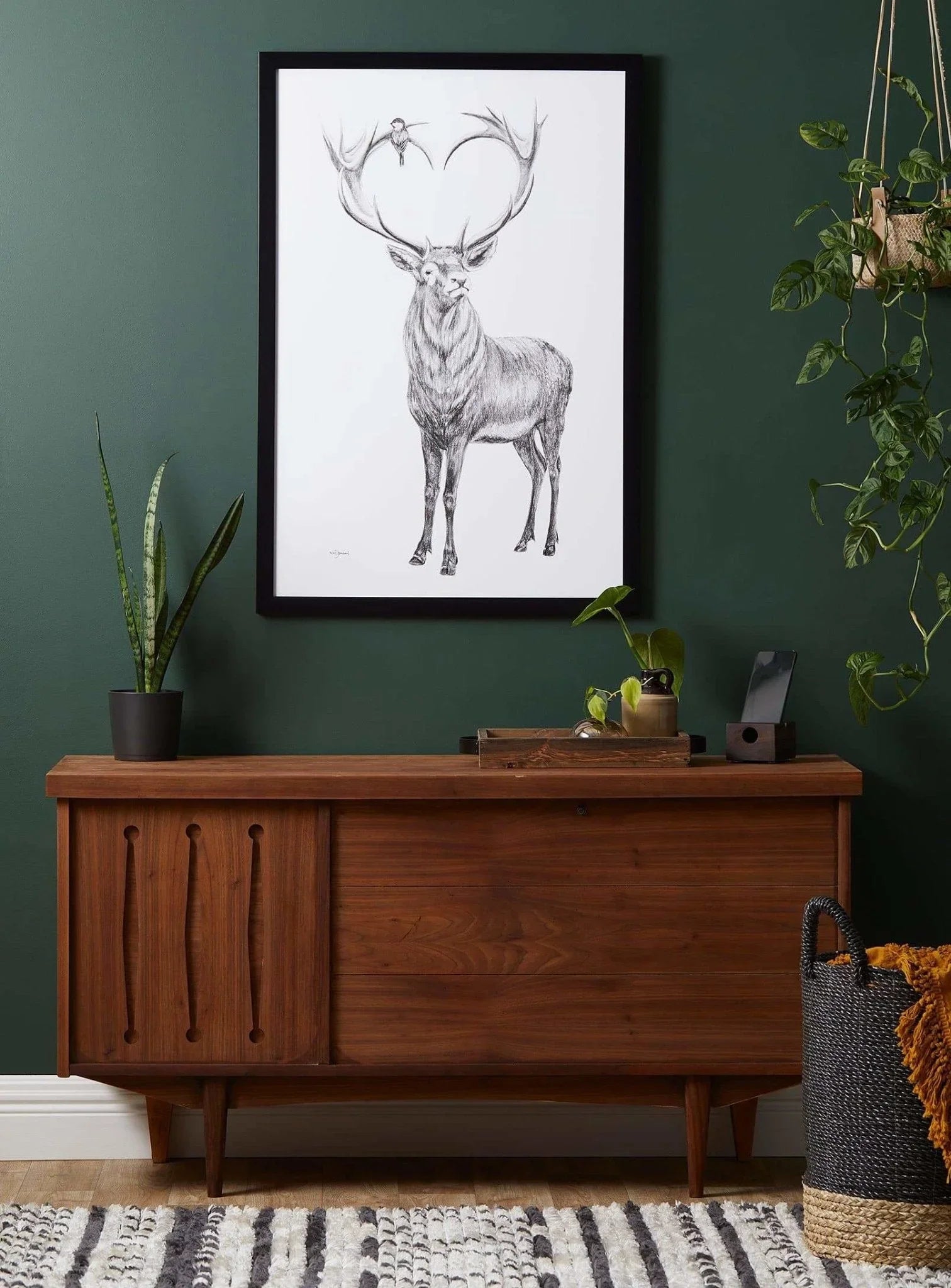 Framed deer art with heart-shaped antlers hanging on dark green wall above wooden console