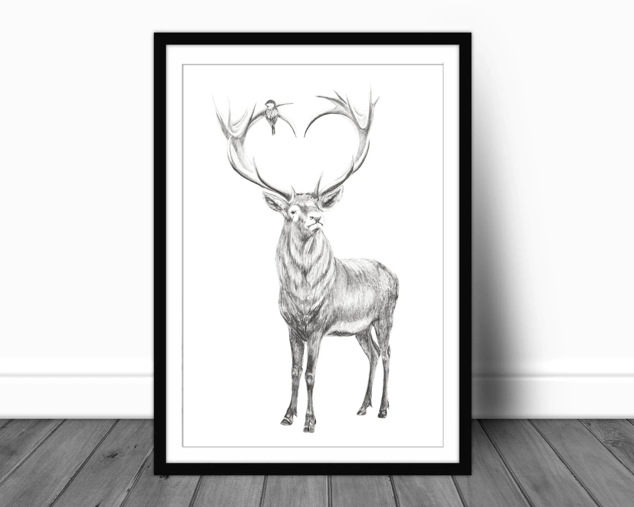 Deer with heart-shaped antlers art print in black frame on wooden floor