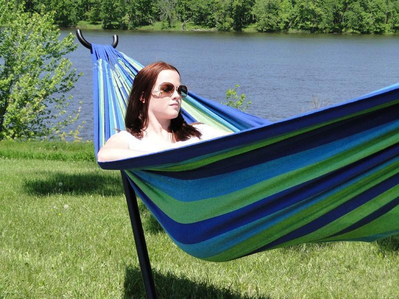 Woman relaxing in blue green Brazilian style double hammock with universal hammock stand by a lake