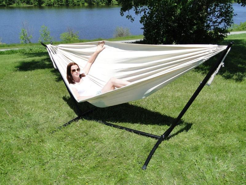 Woman relaxing in a cream Brazilian style double hammock with universal stand on grass by lake