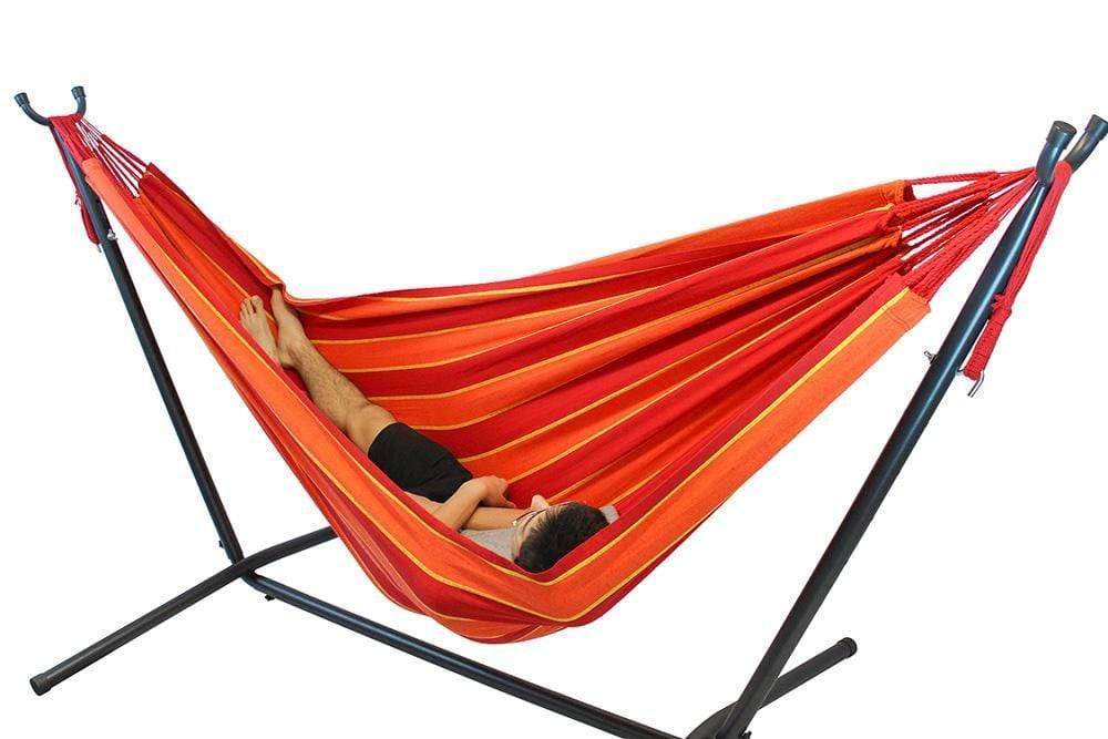 Man relaxing in red, orange, and yellow double hammock with stand on white background