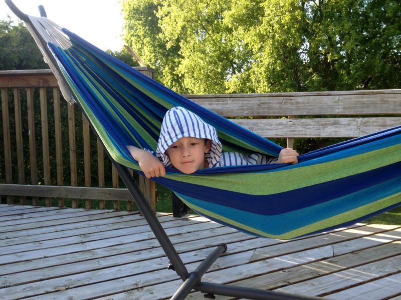 Brazilian hammock with striped fabric on stand, outdoors on wooden deck, sunny day