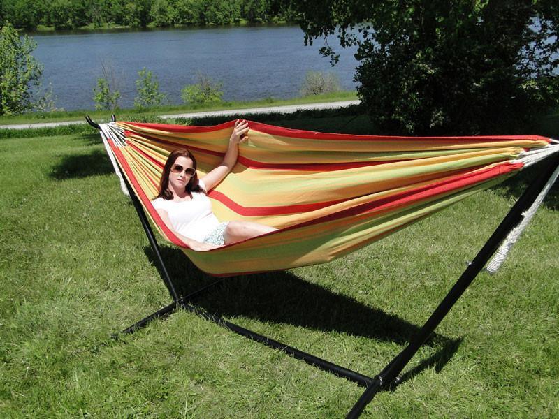 Woman relaxing on a striped hammock with stand outdoors by a river on a sunny day