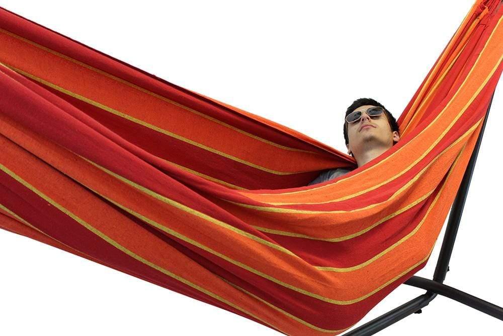 Double hammock with stand in red, orange, and yellow stripes, person relaxing inside