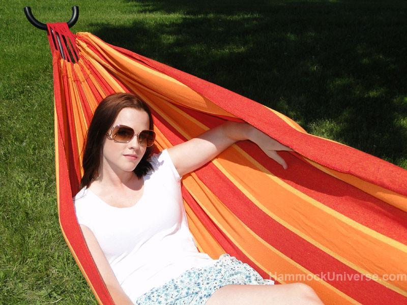 Woman relaxing in a striped Brazilian double hammock outdoors on green grass