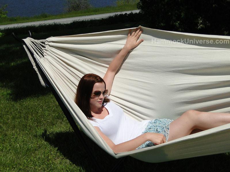 Woman relaxing in a cream Brazilian double hammock outdoors on a sunny grassy lawn