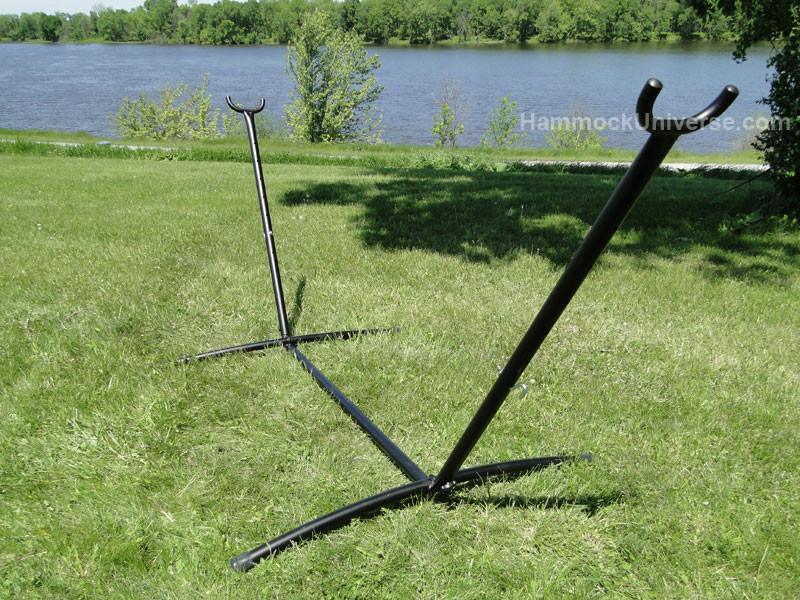 Metal hammock stand on green grass near lake with trees in background