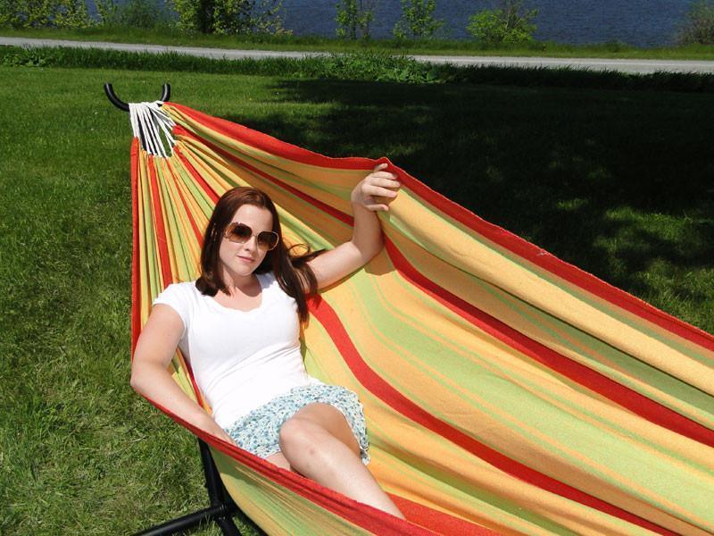 Woman relaxing on striped hammock outdoors, summer day, green grass, casual outfit, sunglasses