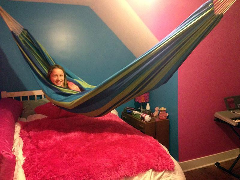 Girl in green and blue hammock above pink bed in colorful bedroom with blue and pink walls
