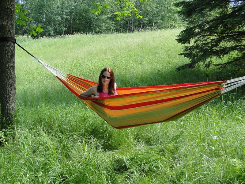 Woman relaxing in red and orange striped hammock outdoors in grassy field