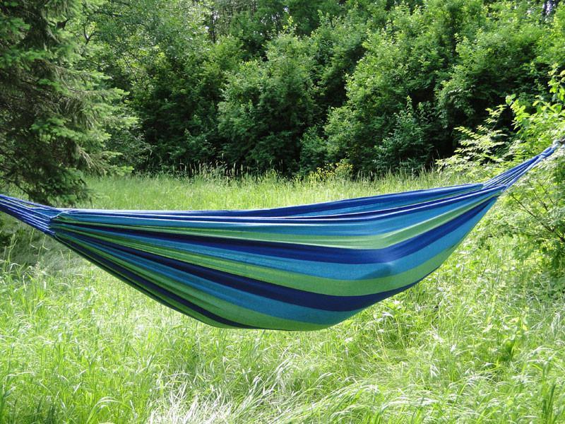 Blue and green striped Brazilian-style double hammock hanging outdoors in grassy field