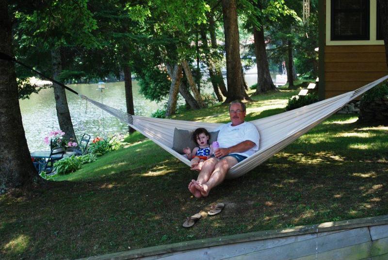Man and child relaxing on a Brazilian double hammock outdoors by a lake with trees