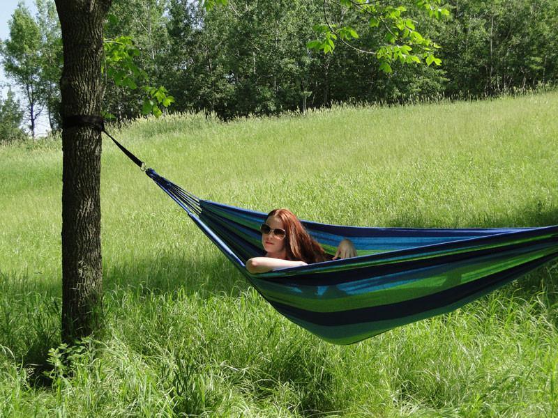 Woman relaxing in blue green Brazilian style double hammock hanging outdoors on grass