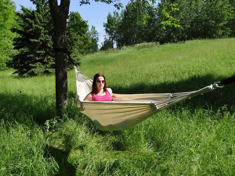 Woman relaxing in a beige Brazilian-style double hammock outdoors on a grassy lawn