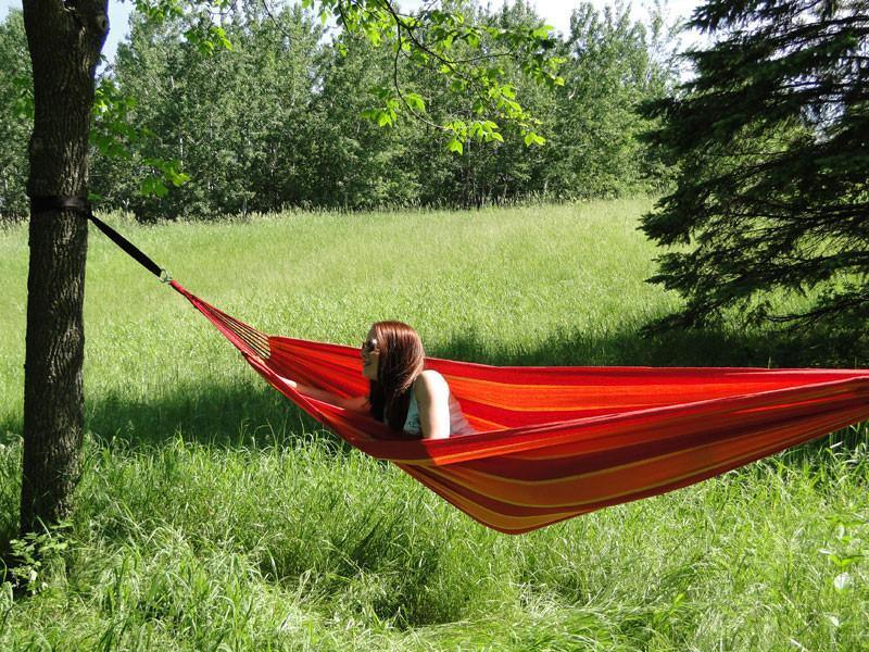 Woman relaxing in a red Brazilian-style double hammock outdoors in a grassy field