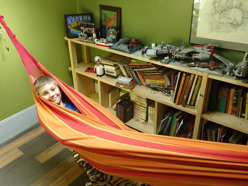 Boy relaxing in a Brazilian double hammock indoors with bookshelves and toys in the background