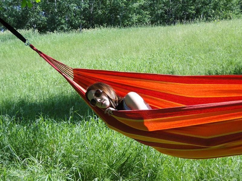 Woman relaxing in a red Brazilian-style double hammock outdoors on green grass