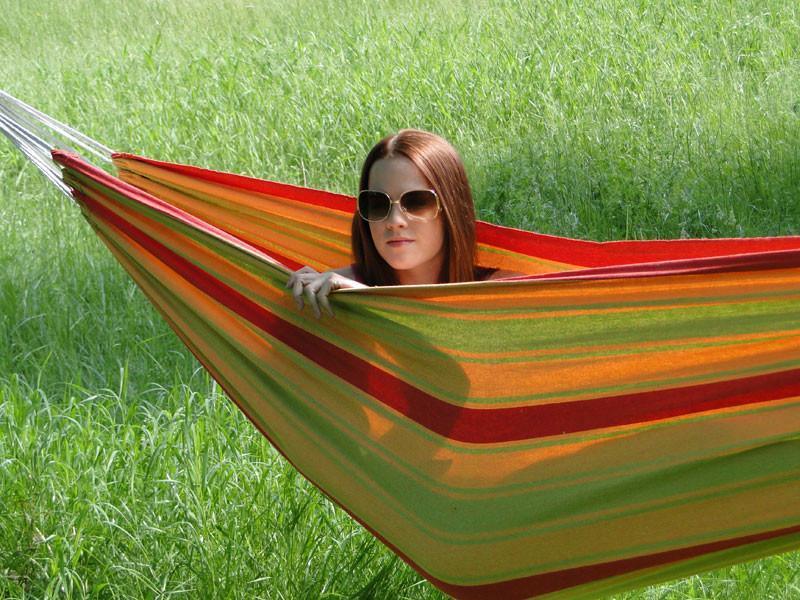 Woman in striped orange hammock relaxing outdoors on green grass field, wearing sunglasses
