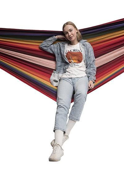 Woman sitting on a double Brazilian hammock with bright multicolored stripes