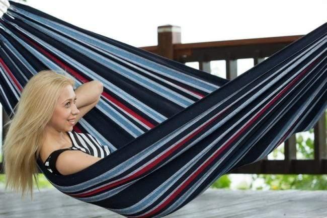 Woman relaxing in blue striped Brazilian hammock on wooden deck outdoors
