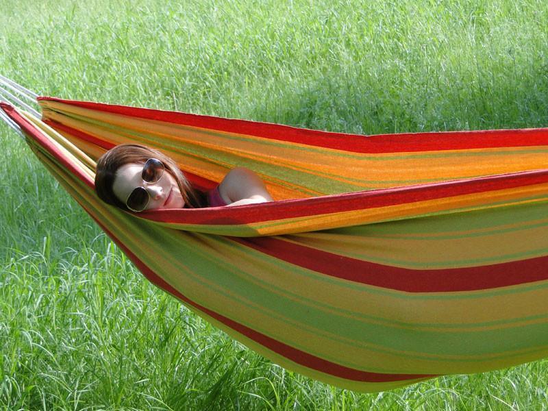 Woman relaxing in striped hammock outdoors on green grass