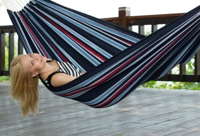 Woman relaxing in striped Brazilian hammock on wooden deck outdoors
