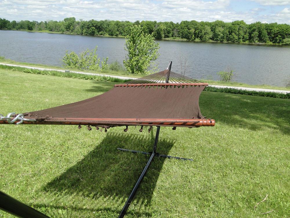 Brown polyester rope hammock on stand in grassy yard near lake and trees