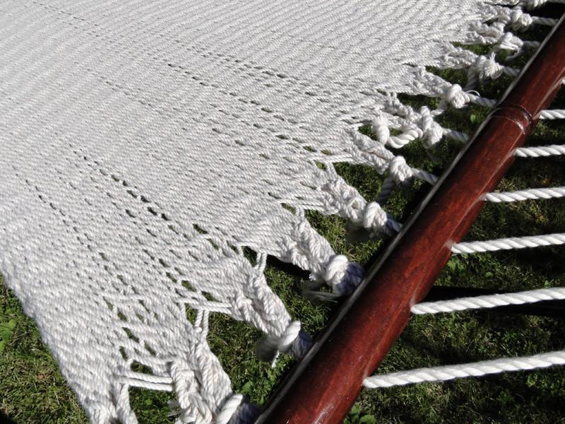 Cream polyester rope hammock with wooden spreader bar on green grass outdoors