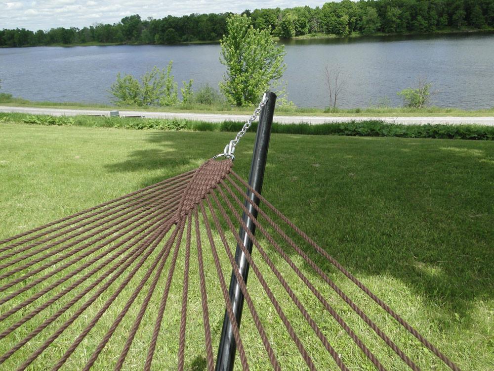 Brown polyester rope hammock on black metal stand by a lake and green lawn