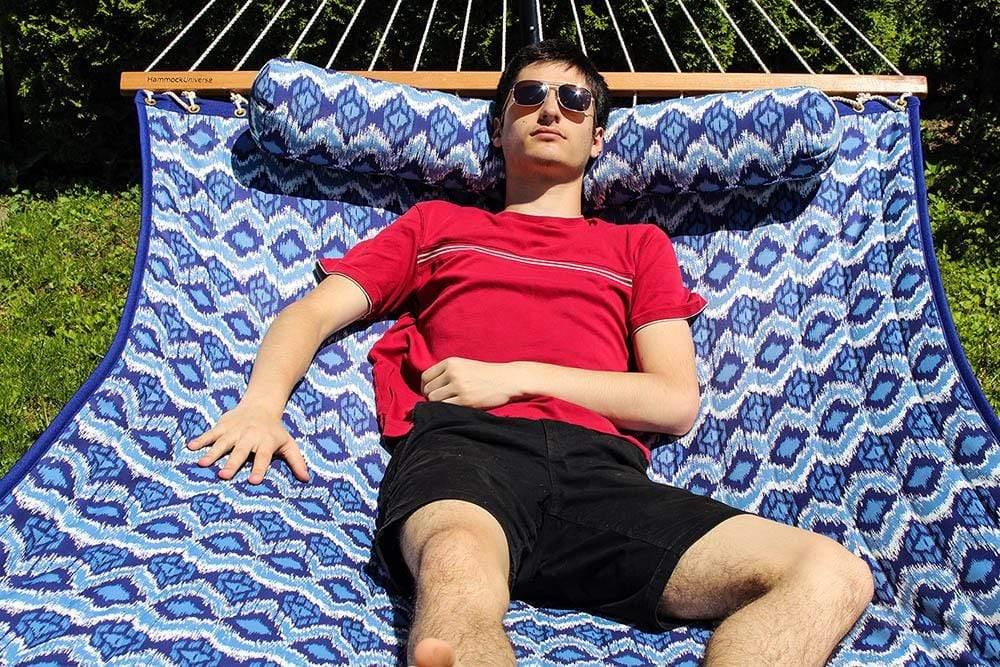 Man relaxing on a blue and white quilted double hammock outdoors