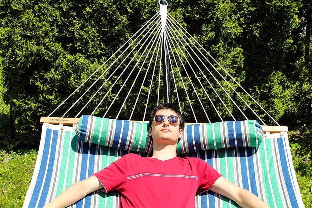 Man relaxing on striped blue and green quilted double hammock outdoors