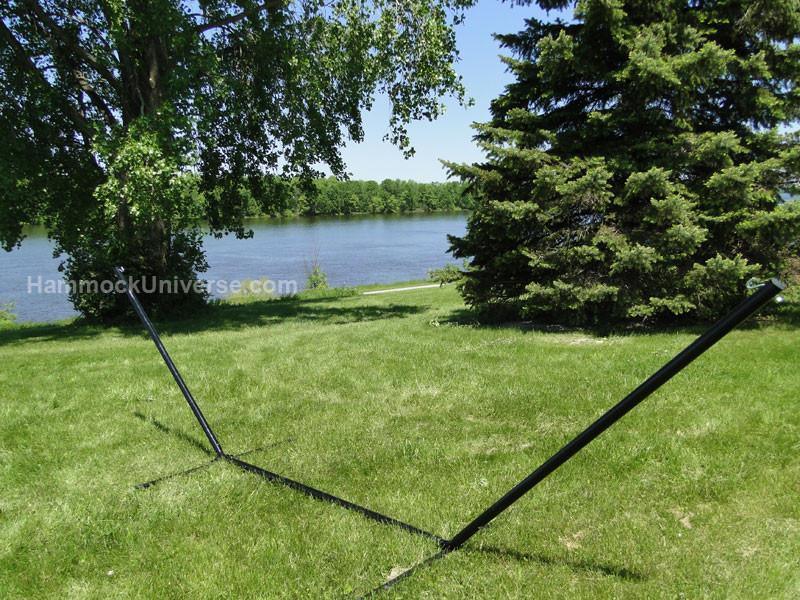 Hammock stand on grassy lawn by river with trees, outdoor relaxation setting