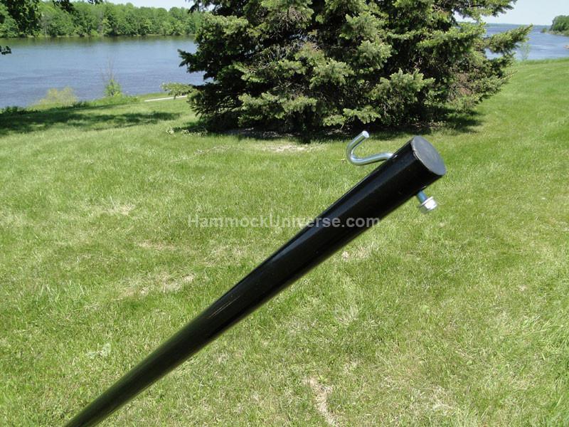 Black metal hammock stand pole with hook outdoors on green grass by a lake
