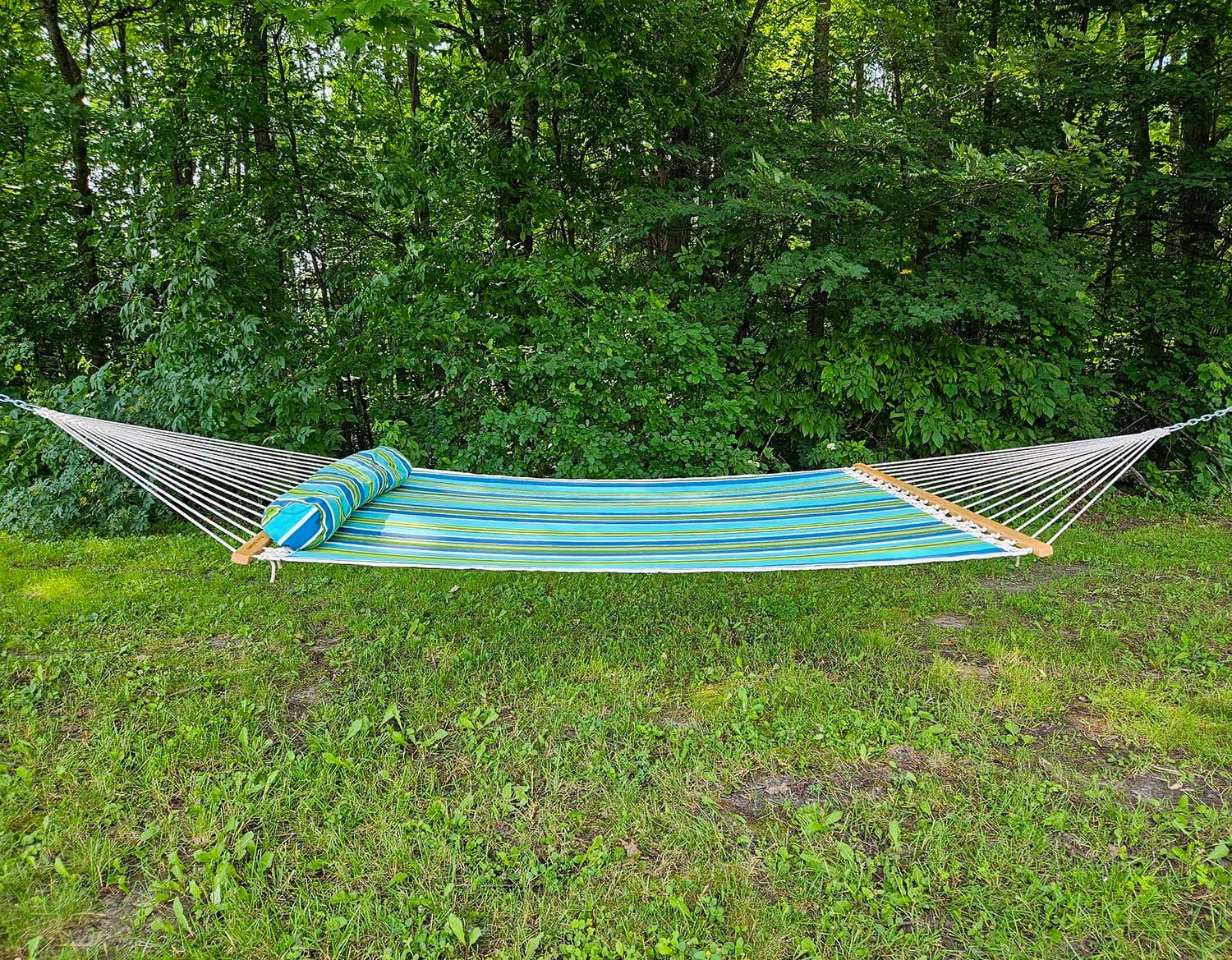 Colorful striped hammock with pillow set up outdoors on green grass near dense trees