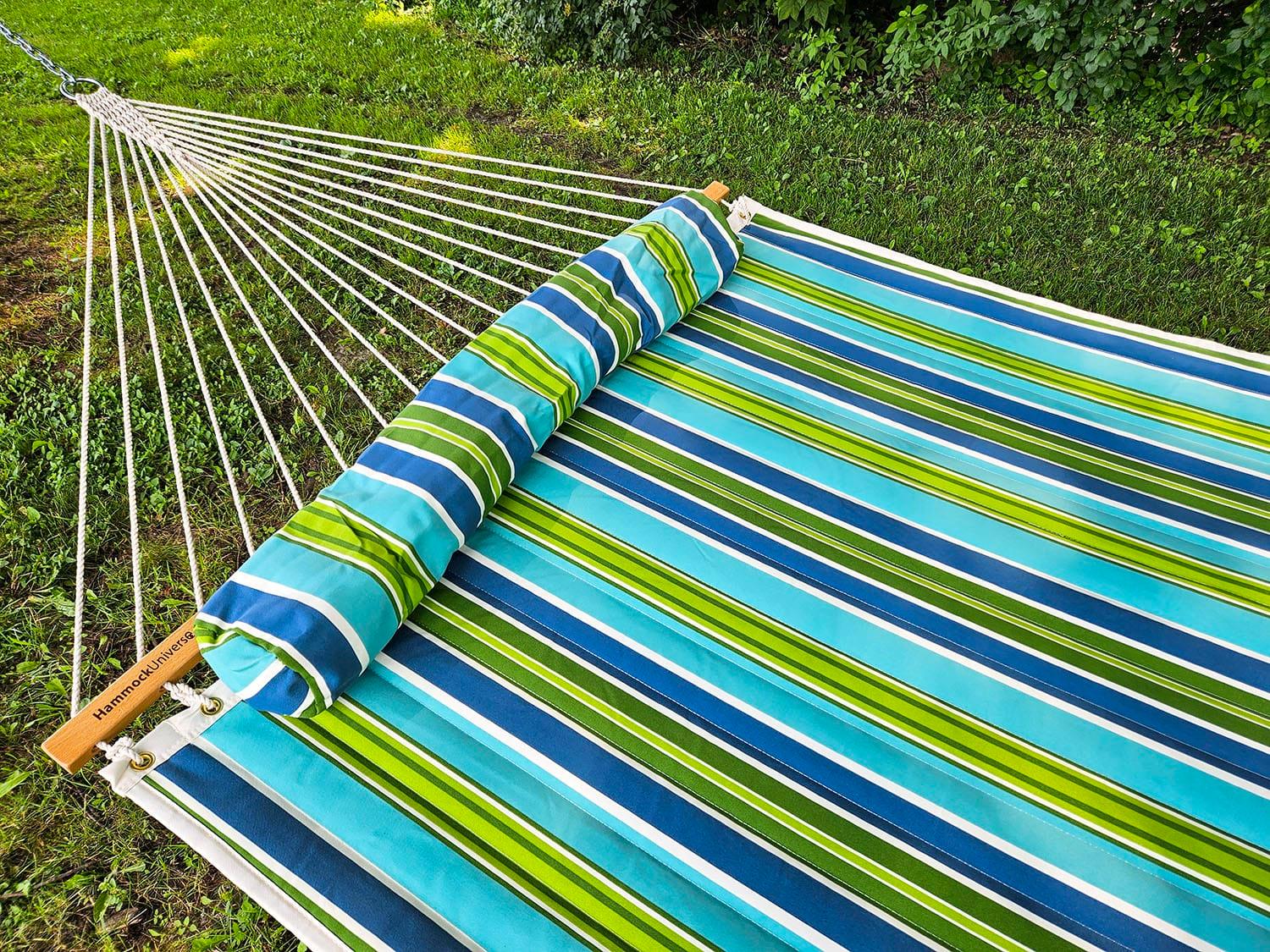 Outdoor hammock with blue and green striped fabric on grass, backyard garden setting