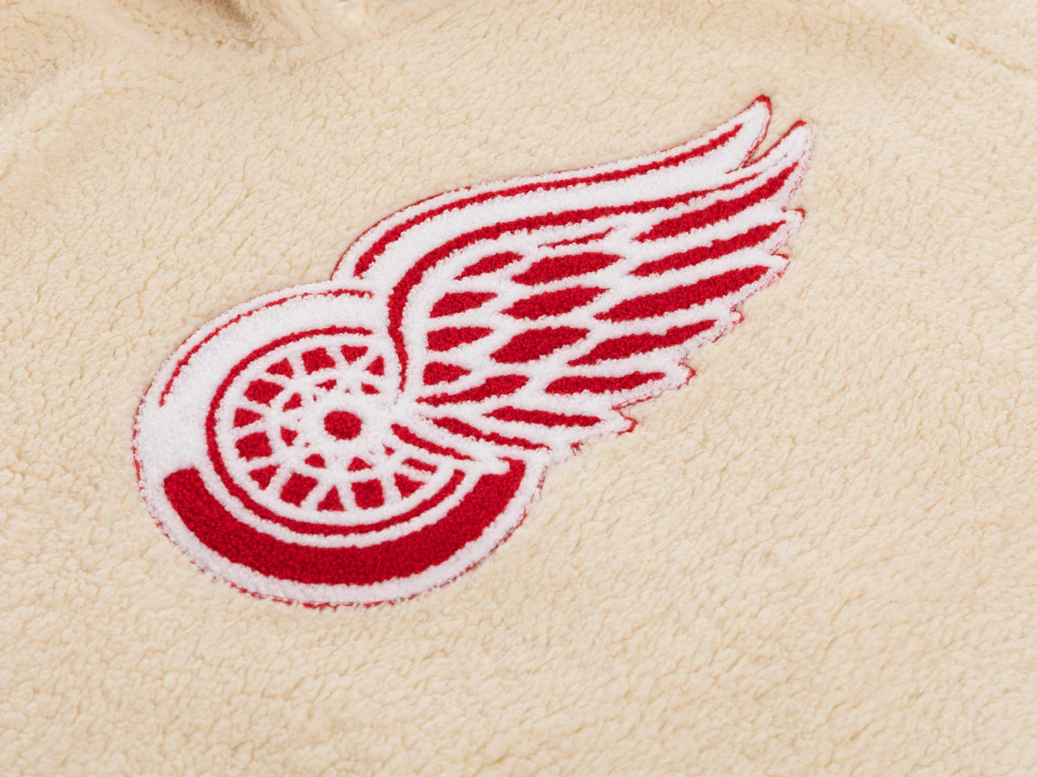 Red winged wheel logo embroidered on beige sherpa fleece fabric