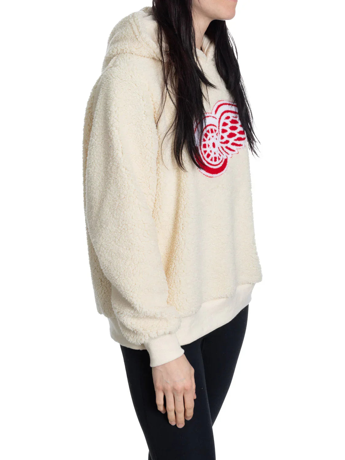 Woman wearing cream sherpa hoodie with red Detroit Red Wings logo on front