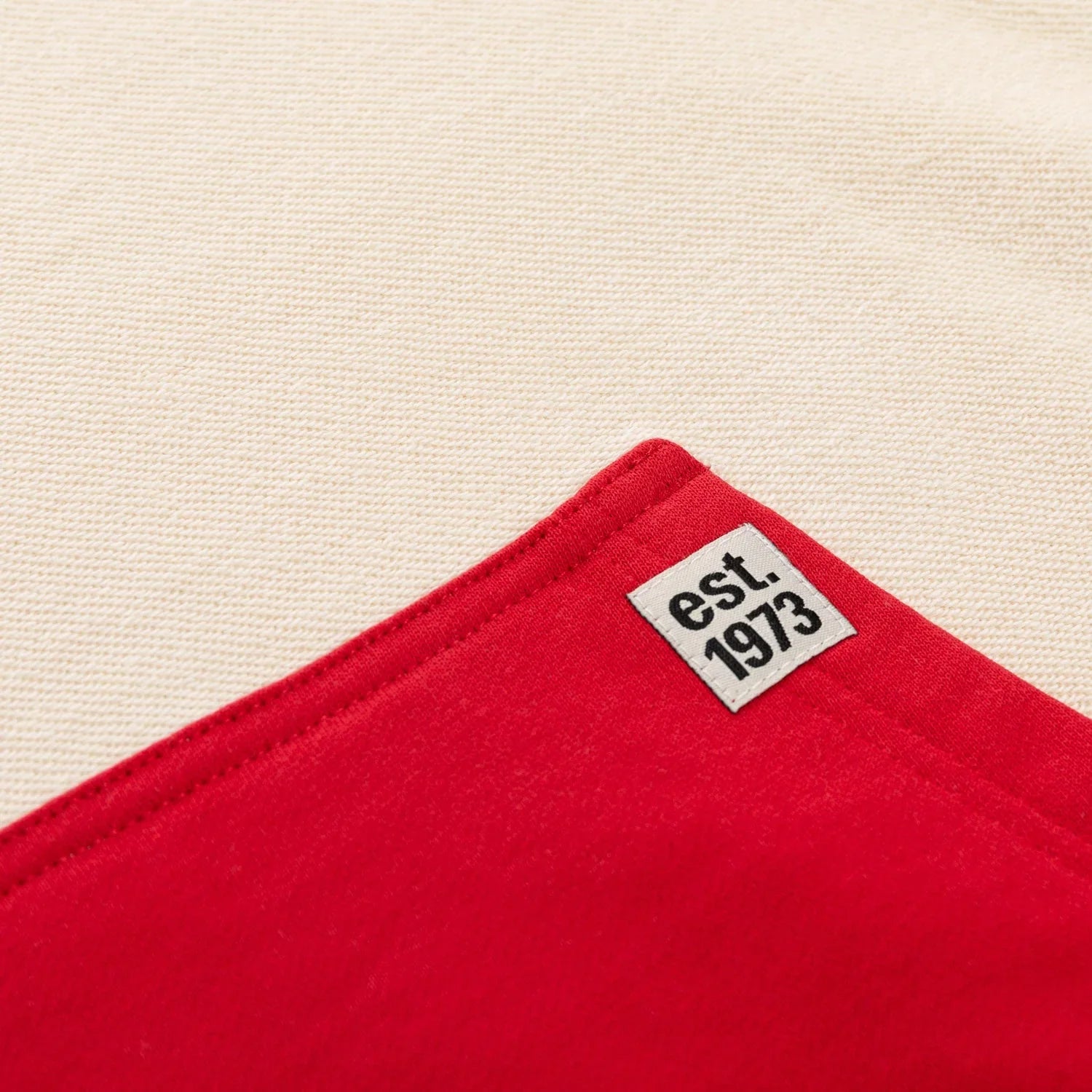Close-up of red hoodie pocket with est. 1973 label on cream fabric background