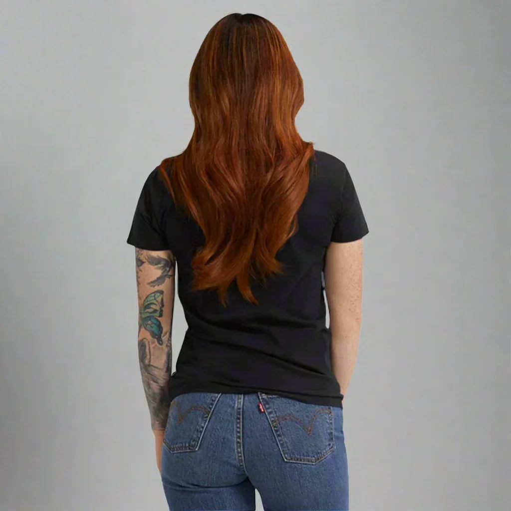 Woman with long red hair, tattooed arm, black t-shirt, and blue jeans seen from behind