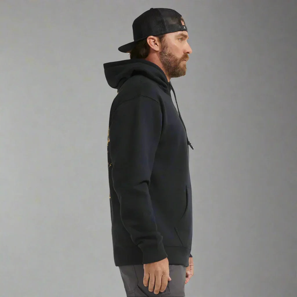 Man in black hoodie and backwards cap standing in profile against grey background
