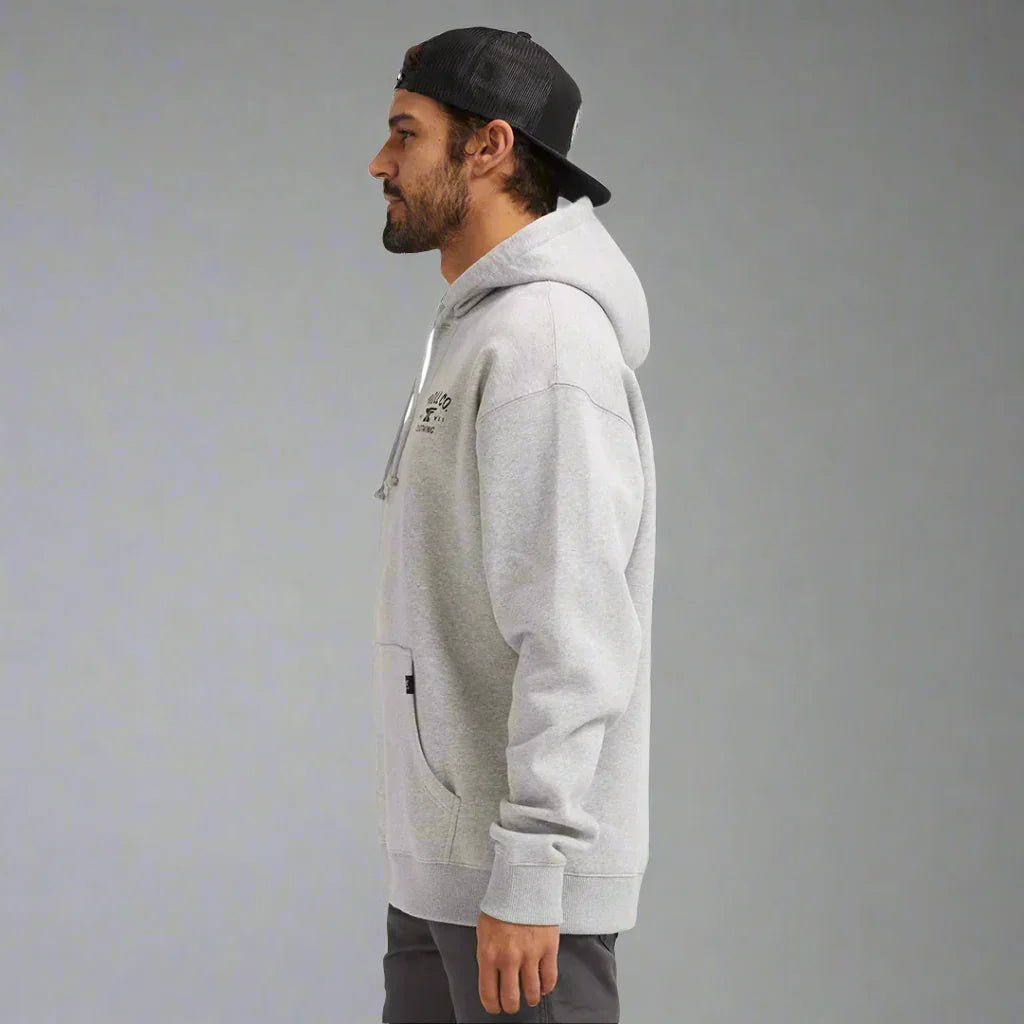 Man in gray hoodie and black cap standing sideways on plain background