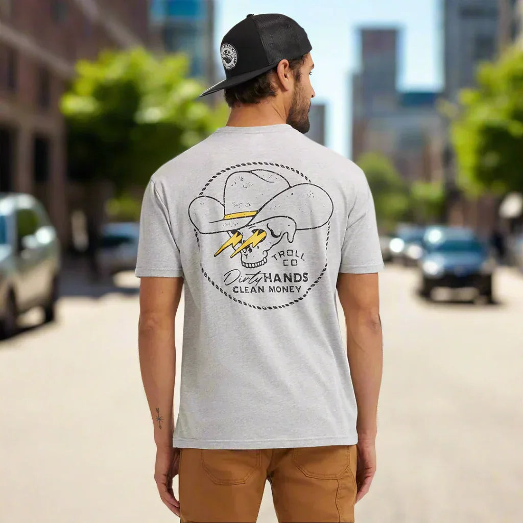 Man wearing graphic t-shirt with skull cowboy hat Dirty Hands Clean Money logo on city street