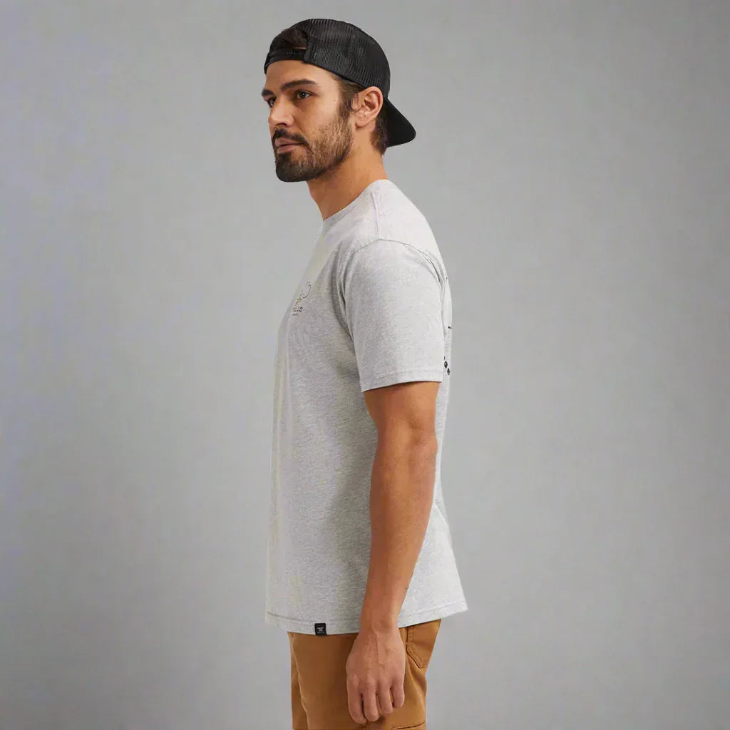 Man in grey t-shirt and tan pants wearing black cap, side profile on plain background
