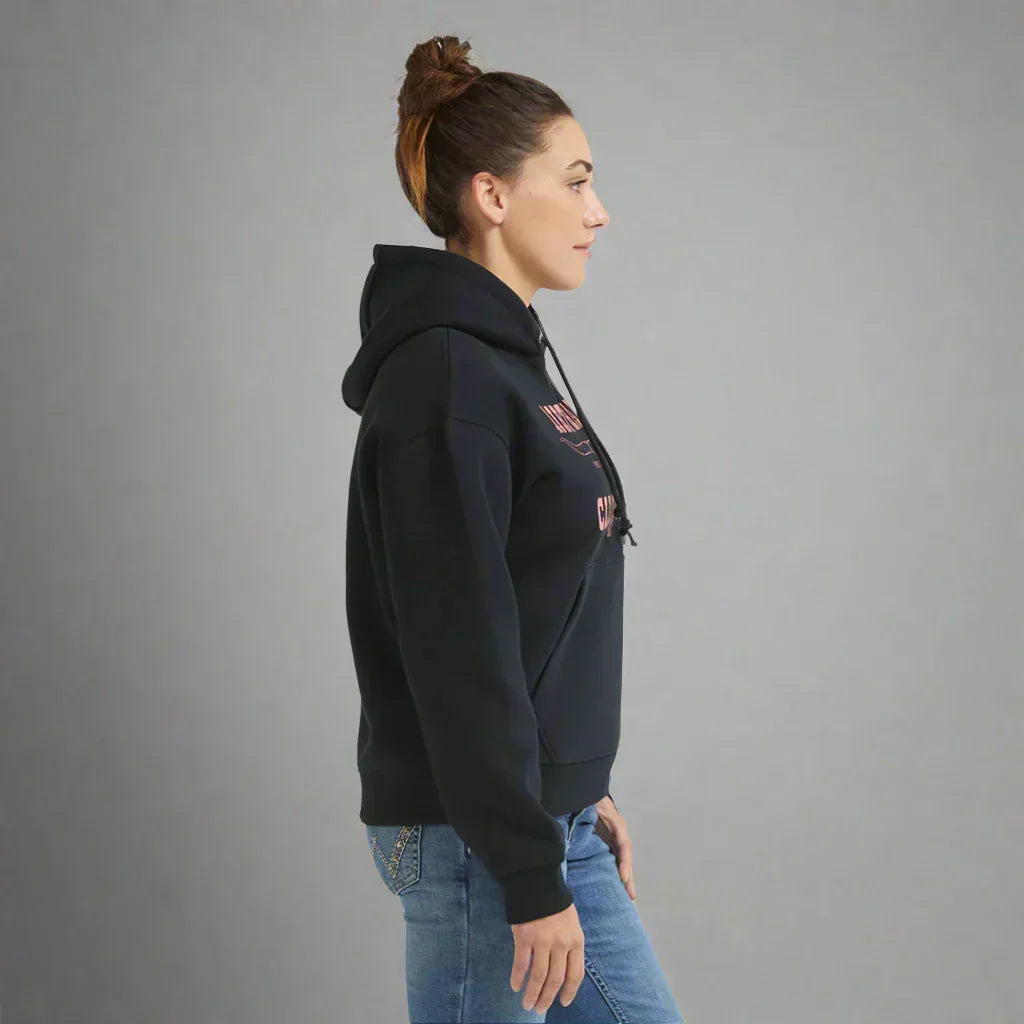 Woman in black hooded sweatshirt and blue jeans standing sideways, grey background
